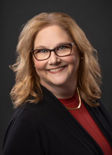 Smiling woman with glasses and wavy blonde hair in a professional portrait.